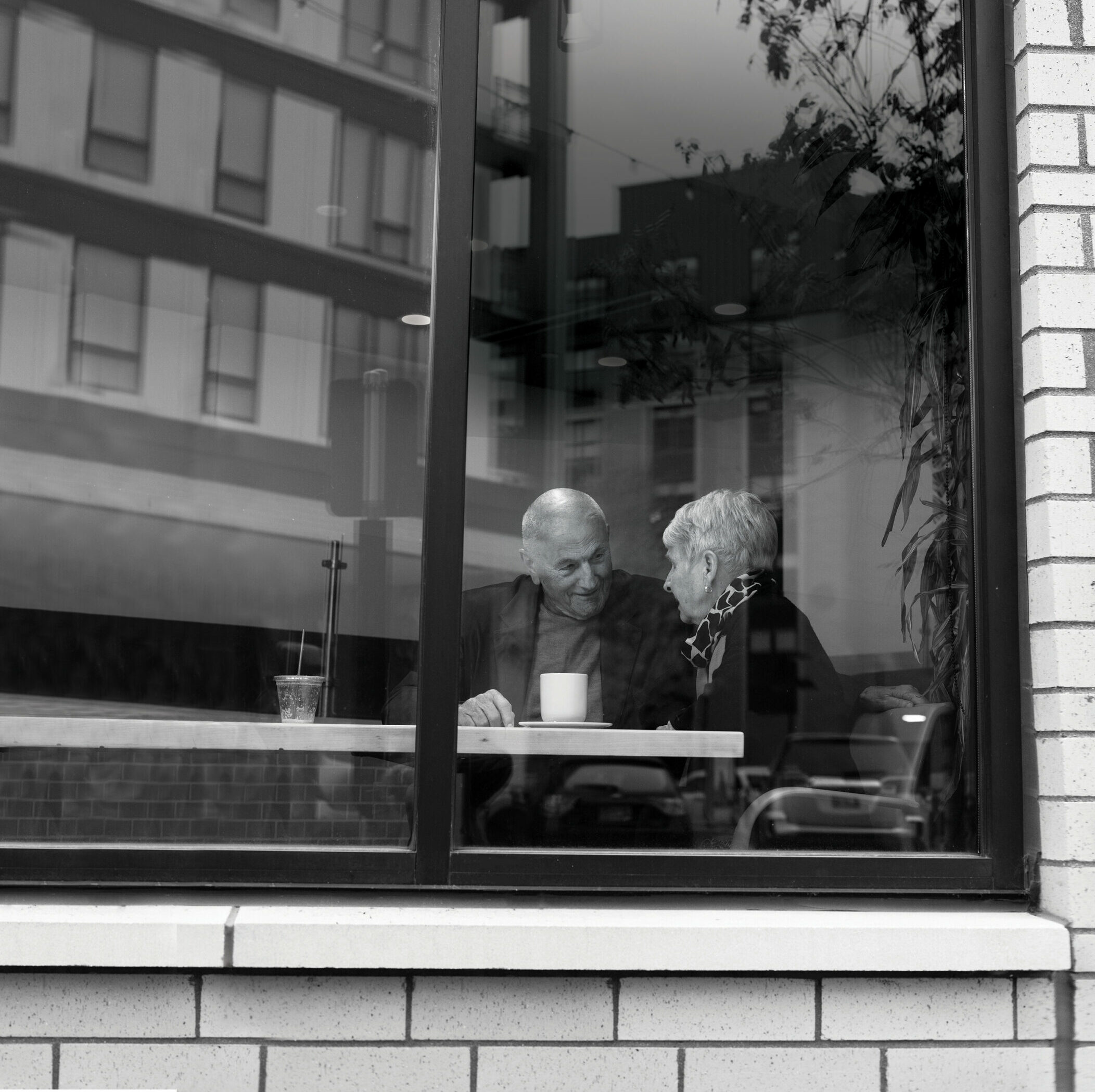 view from sidewalk of a senior couple chatting over coffee in a cafe